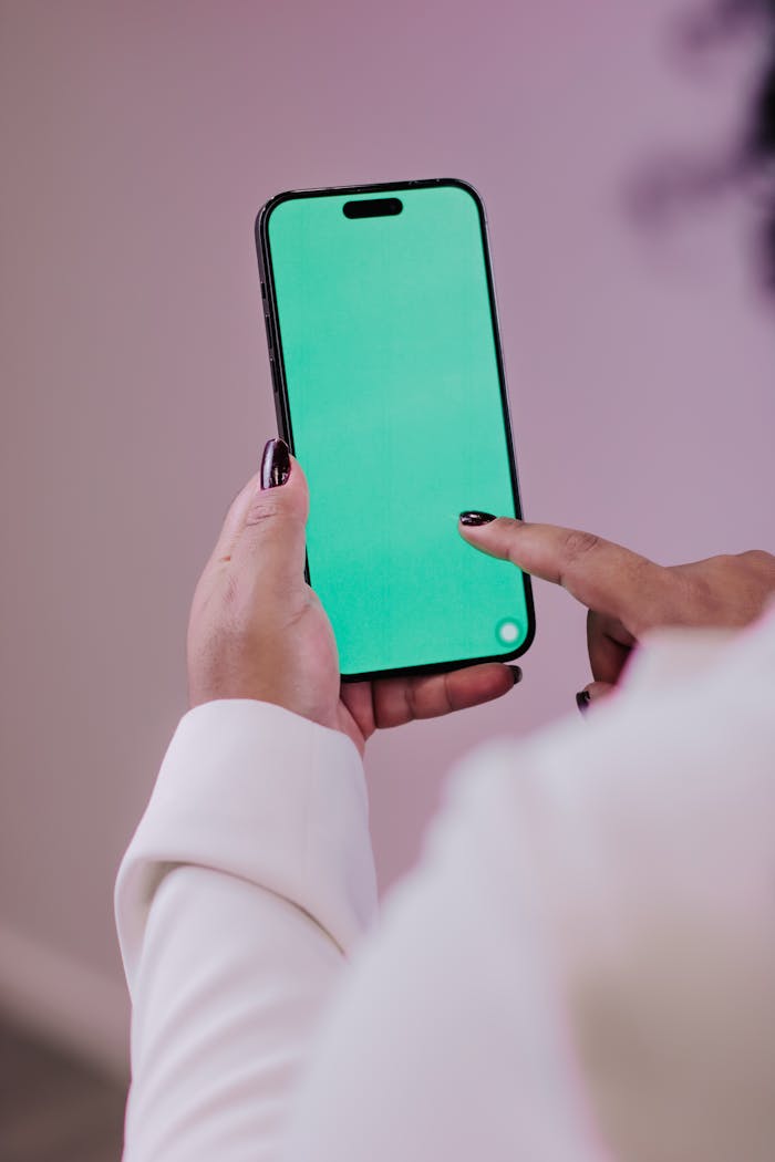 Person using a smartphone with a green screen for editing or mockup purposes.